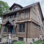 Two painters working on the exterior of a house with ladders and scaffolding
